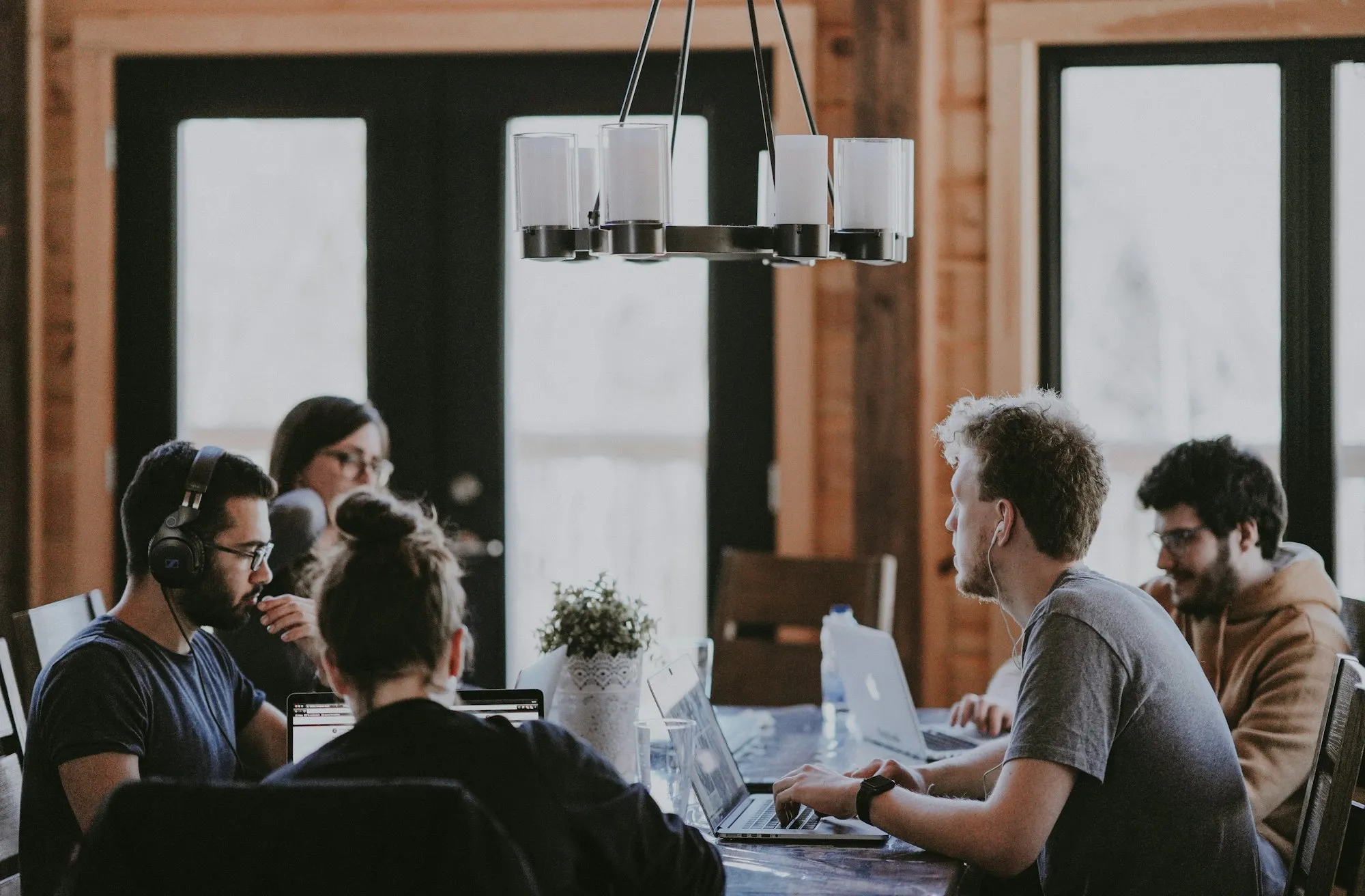 A small team working together on laptops around a wooden table in a bright, wood-panelled room.