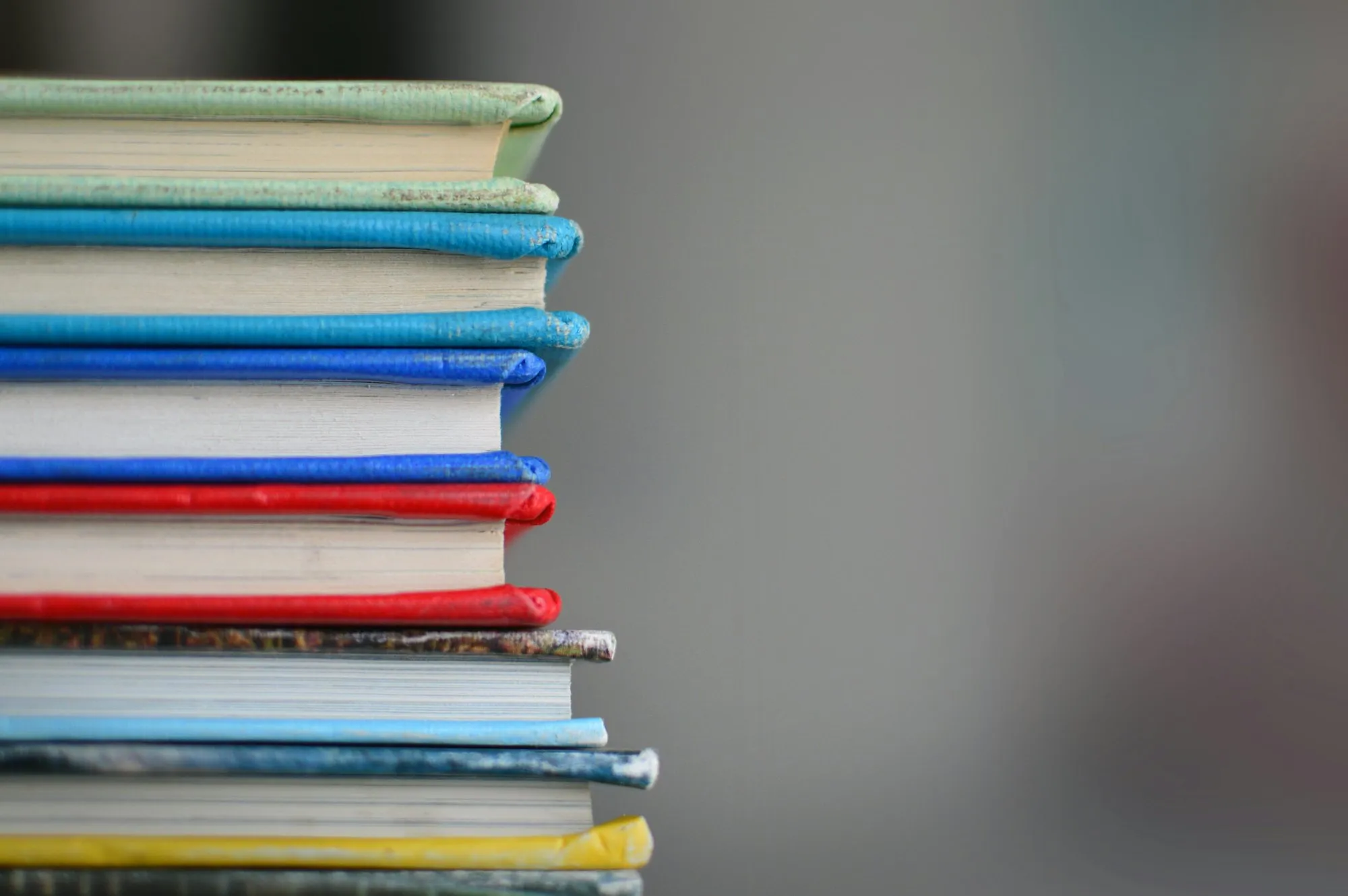 A stack of worn, colourful school textbooks piled one on top of another.