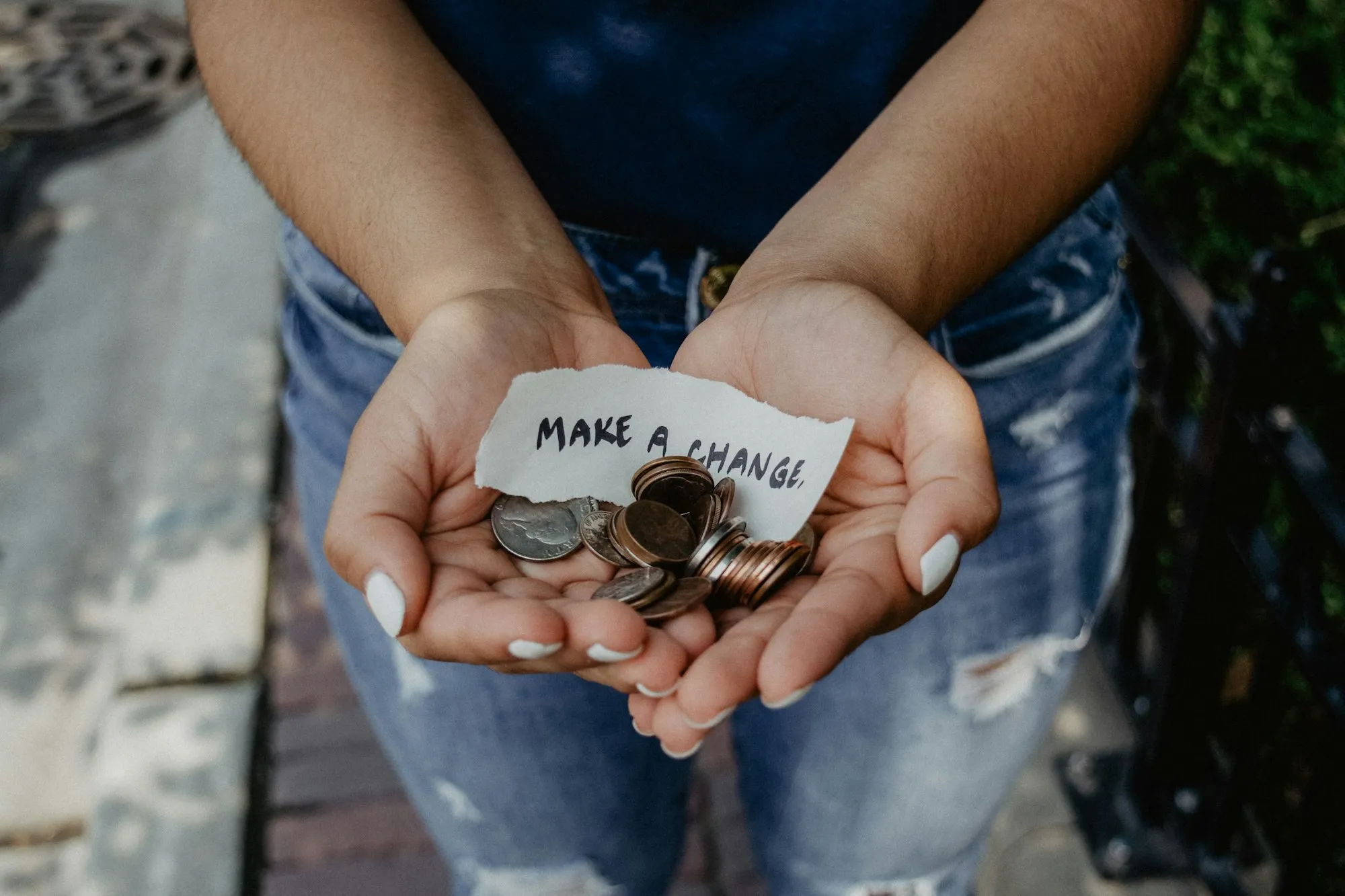 Two open hands holding a small pile of coins and a torn paper note that reads “make a change”.